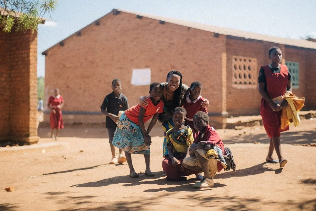 A teammate with schoolchildren outside the brick school at Chilinza Village